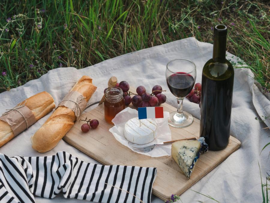 A glass of deep red Bordeaux wine next to a wooden platter filled with an assortment of French cheeses