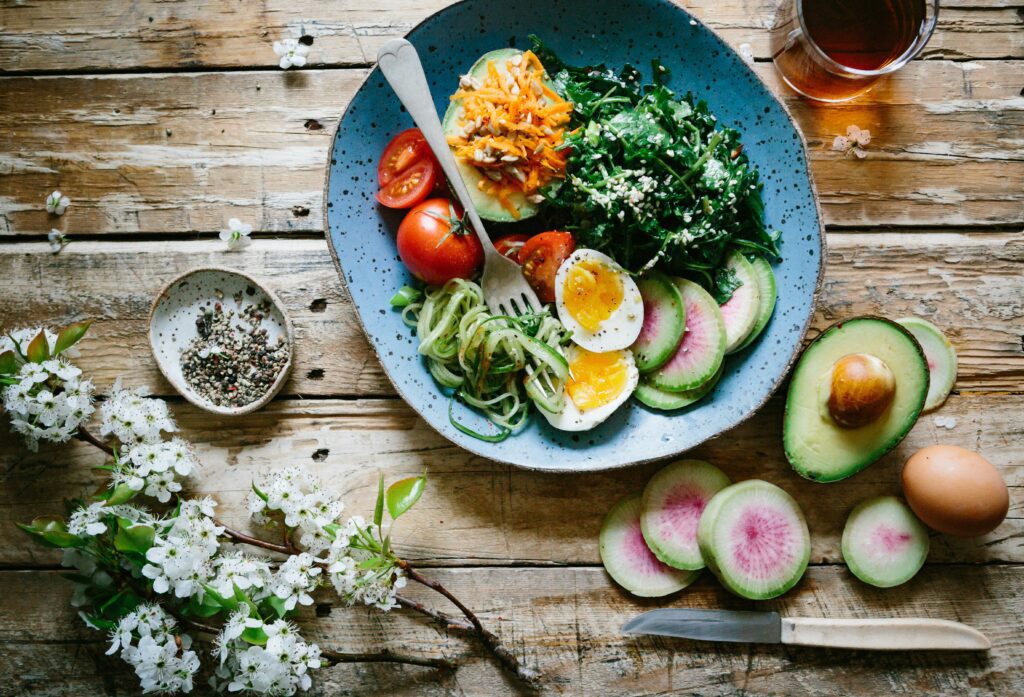 Colorful plate of healthy foods with avocado, leafy greens, cherry tomatoes, grilled chicken, and quinoa.