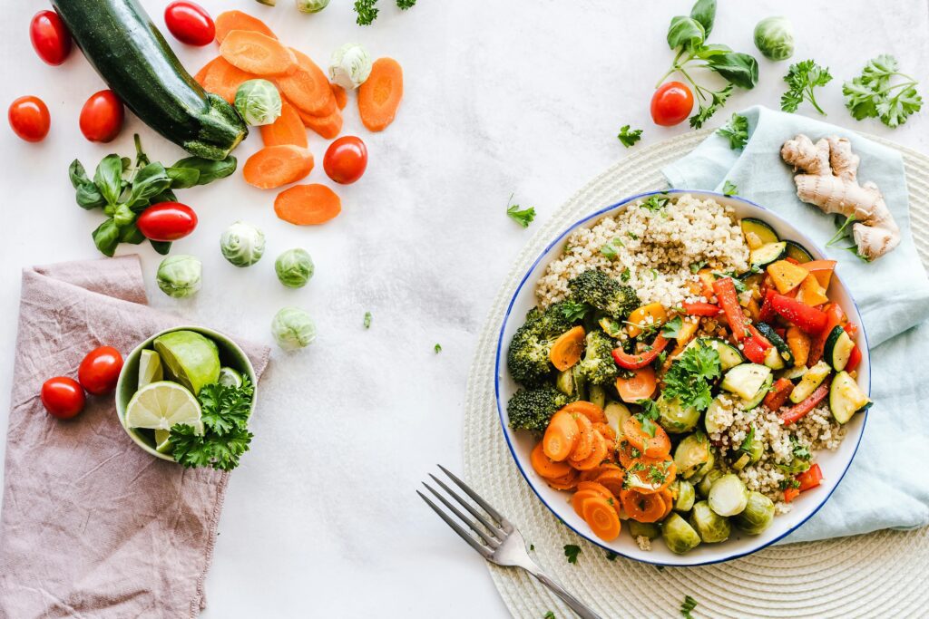 Assiette de quinoa et légumes frais colorés entourée d’ingrédients naturels sur une table claire, vue du dessus.